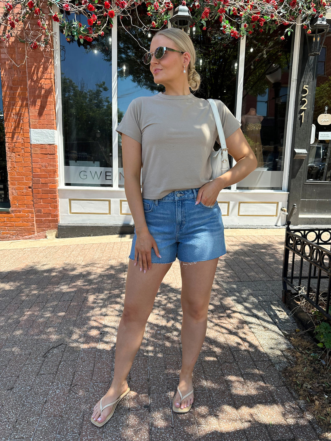 Woman wearing taupe baby tee with medium wash denim shorts. 