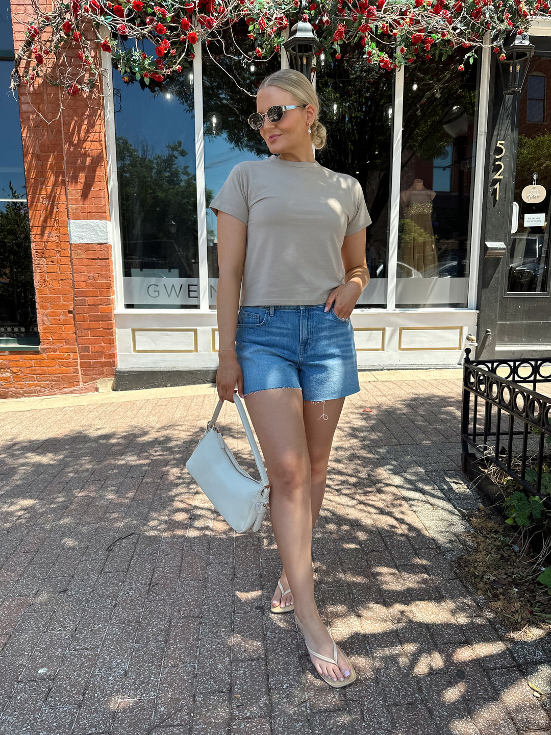 Woman wearing taupe baby tee with medium wash denim shorts. 