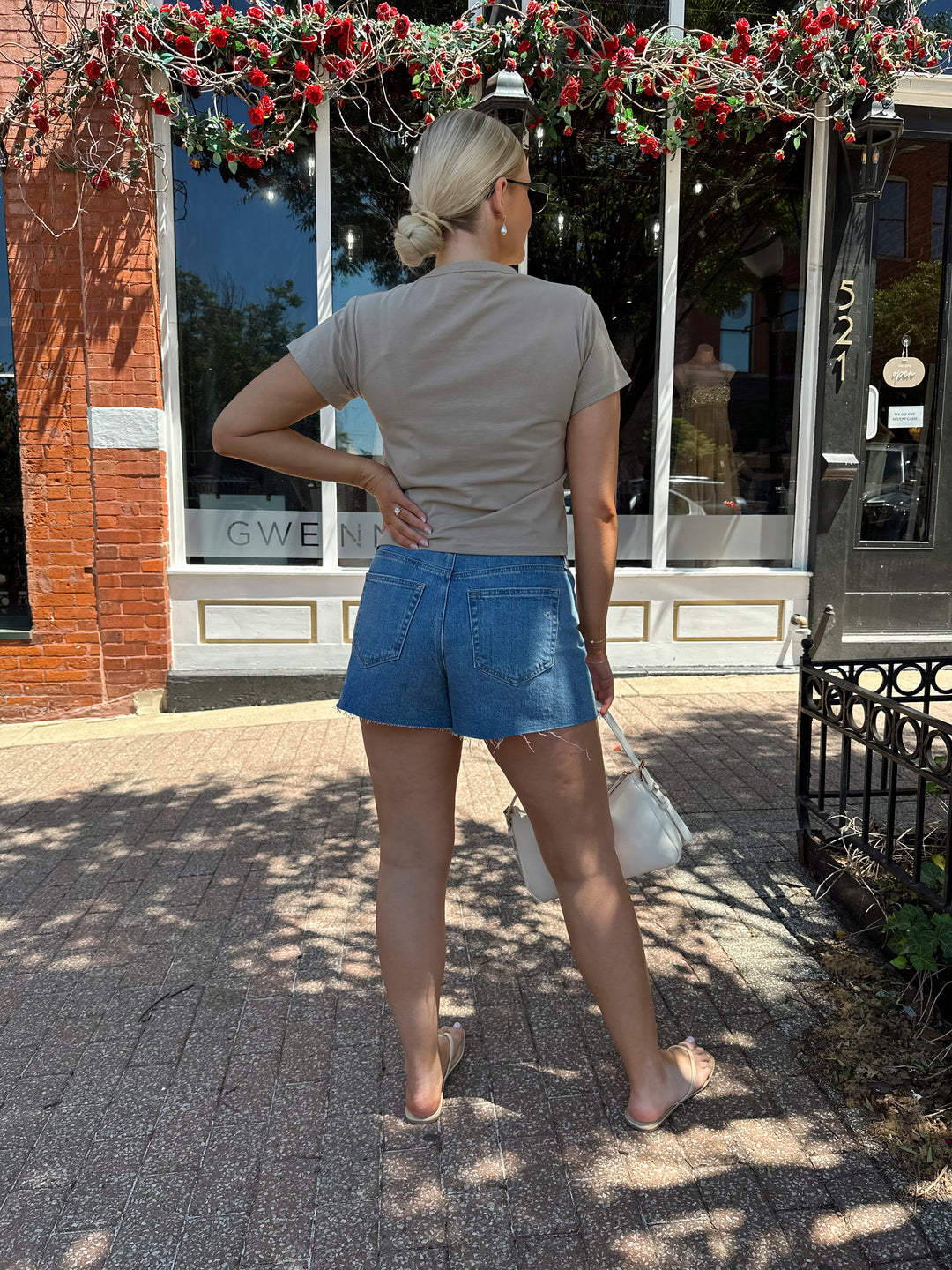 Woman wearing taupe baby tee with medium wash denim shorts. 