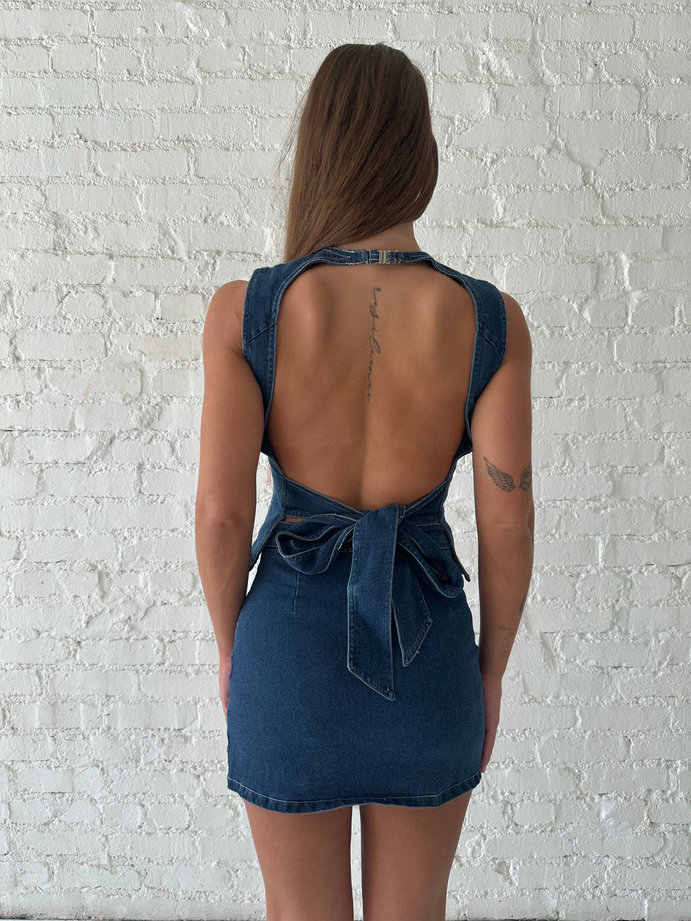 Woman wearing dark wash two piece denim set with open tie back, and mini skirt. 
