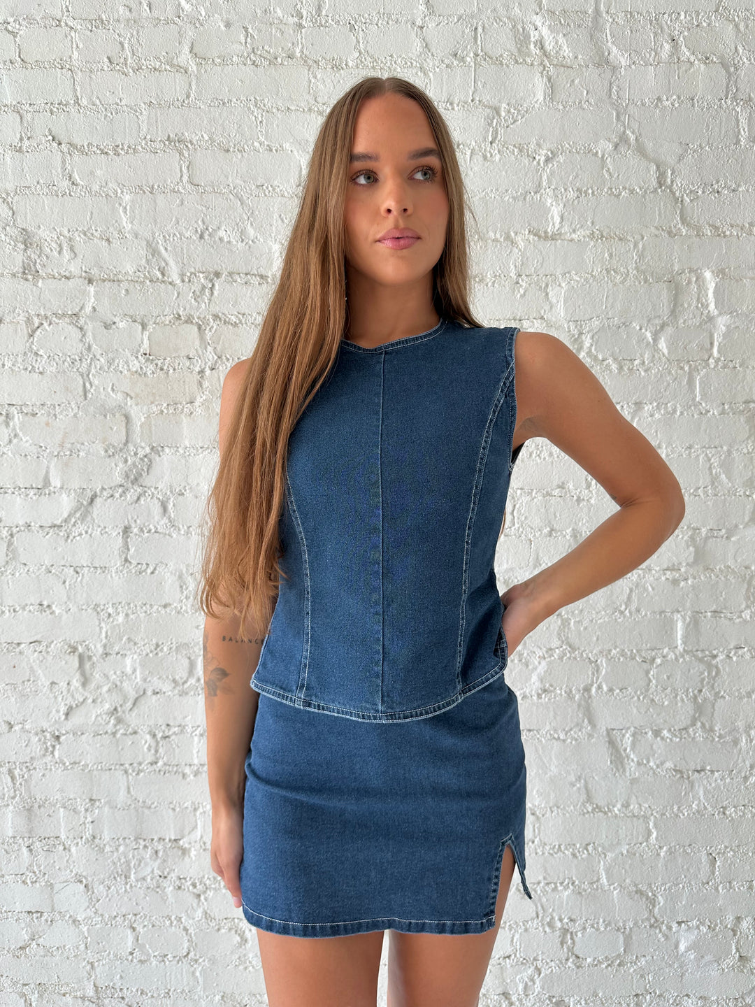 Woman wearing dark wash two piece denim set with open tie back, and mini skirt. 