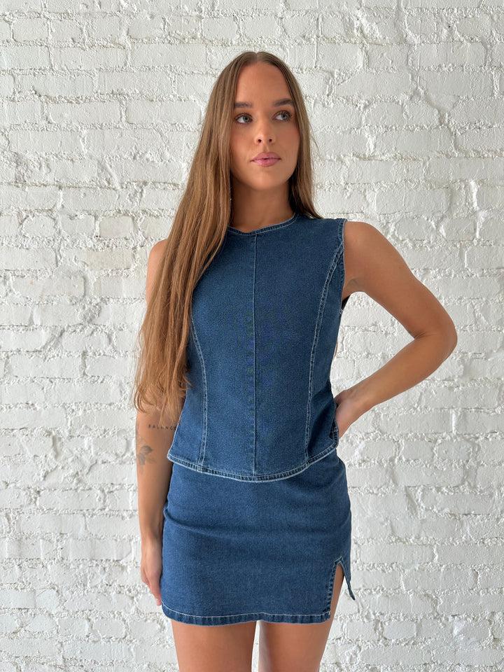 Woman wearing dark wash two piece denim set with open tie back, and mini skirt. 