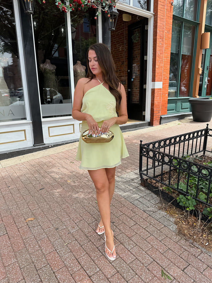 Woman wearing yellow chiffon halter mini dress with beaded detailing, open back with strap detail. 