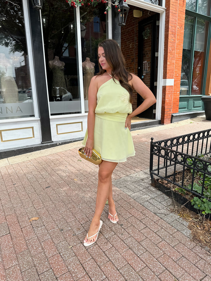 Woman wearing yellow chiffon halter mini dress with beaded detailing, open back with strap detail. 