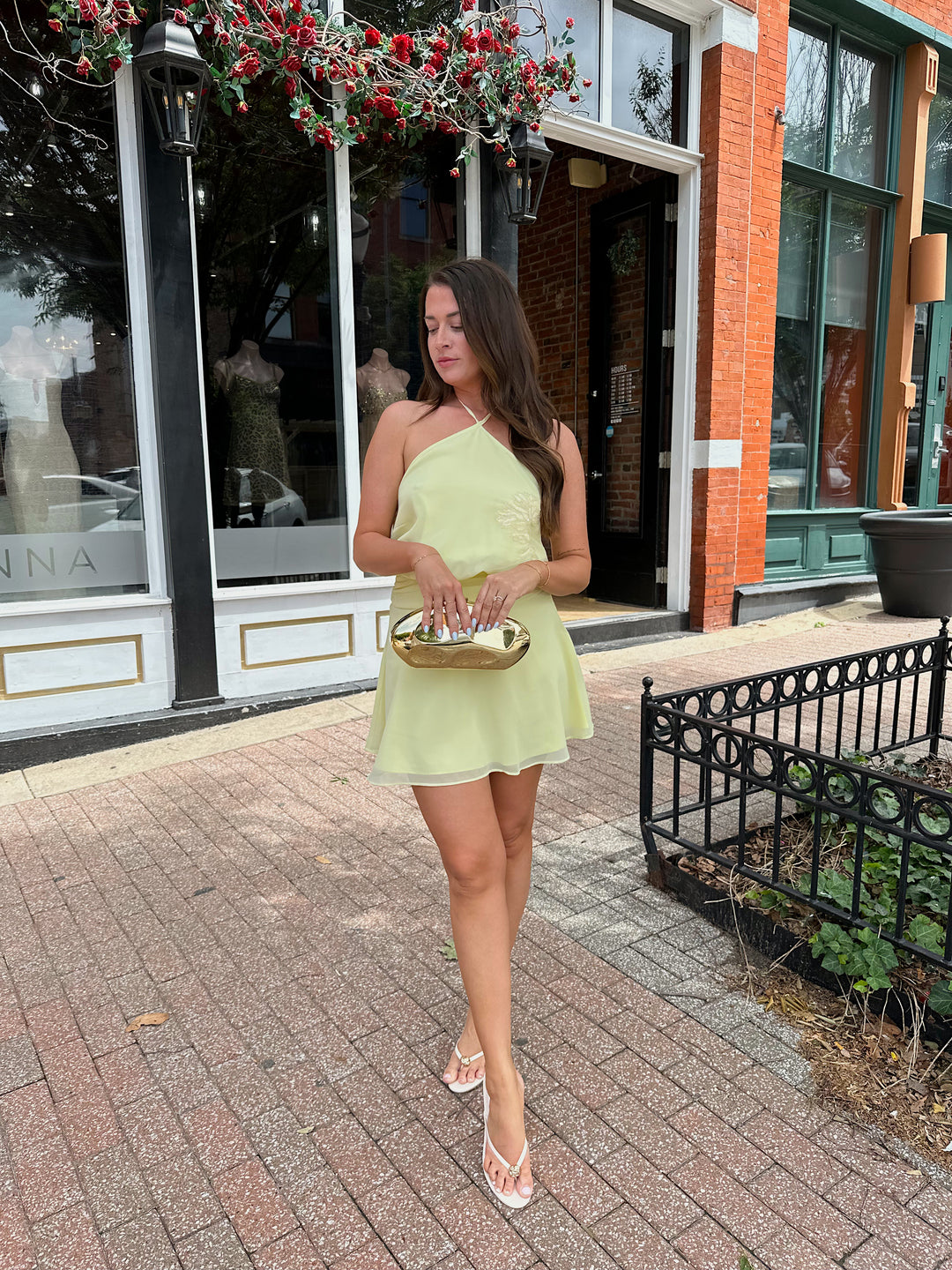 Woman wearing yellow chiffon halter mini dress with beaded detailing, open back with strap detail. 