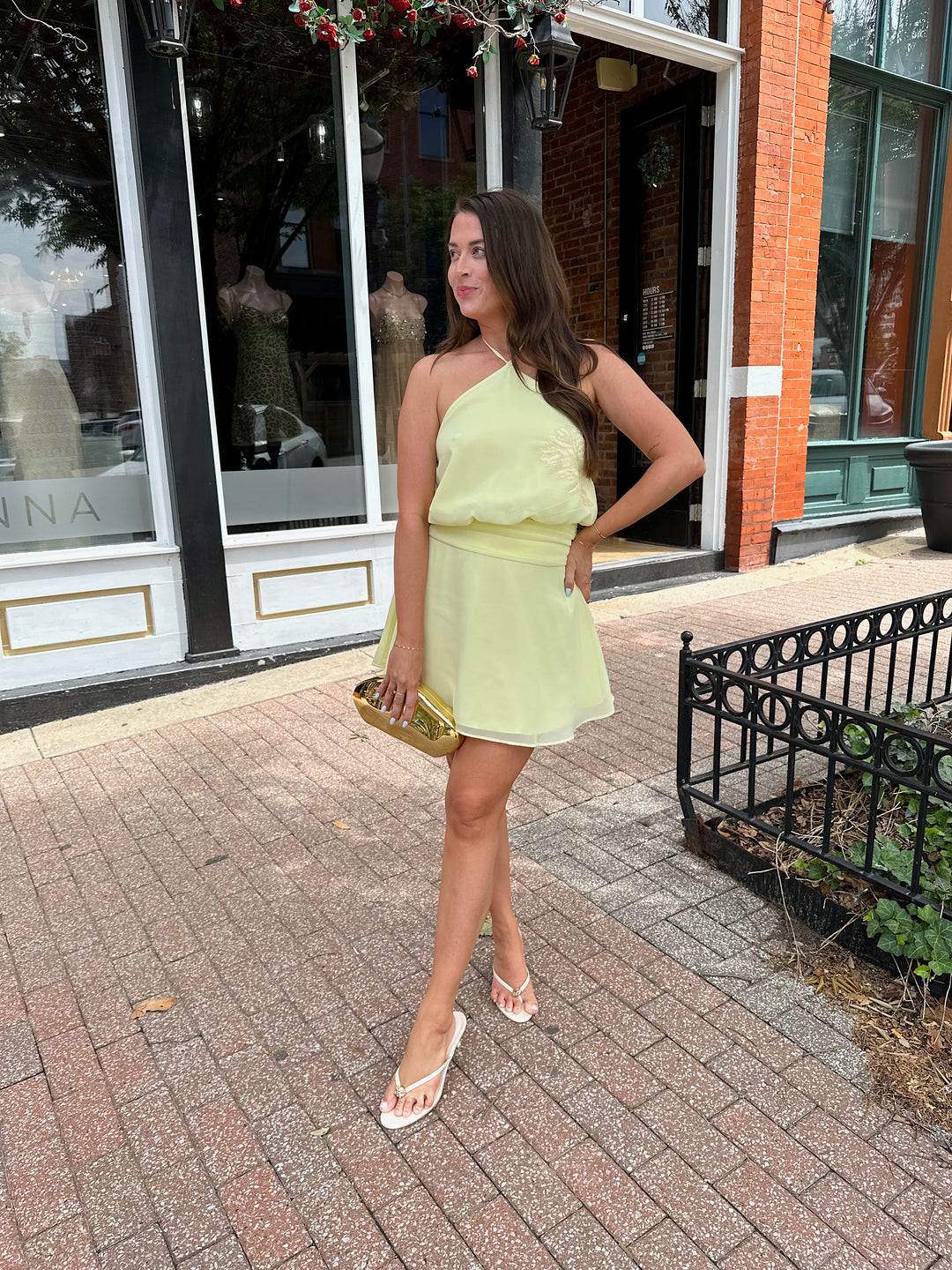 Woman wearing yellow chiffon halter mini dress with beaded detailing, open back with strap detail. 