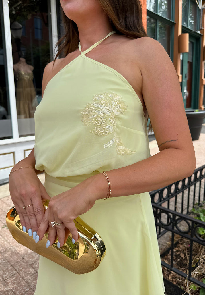 Woman wearing yellow chiffon halter mini dress with beaded detailing, open back with strap detail. 