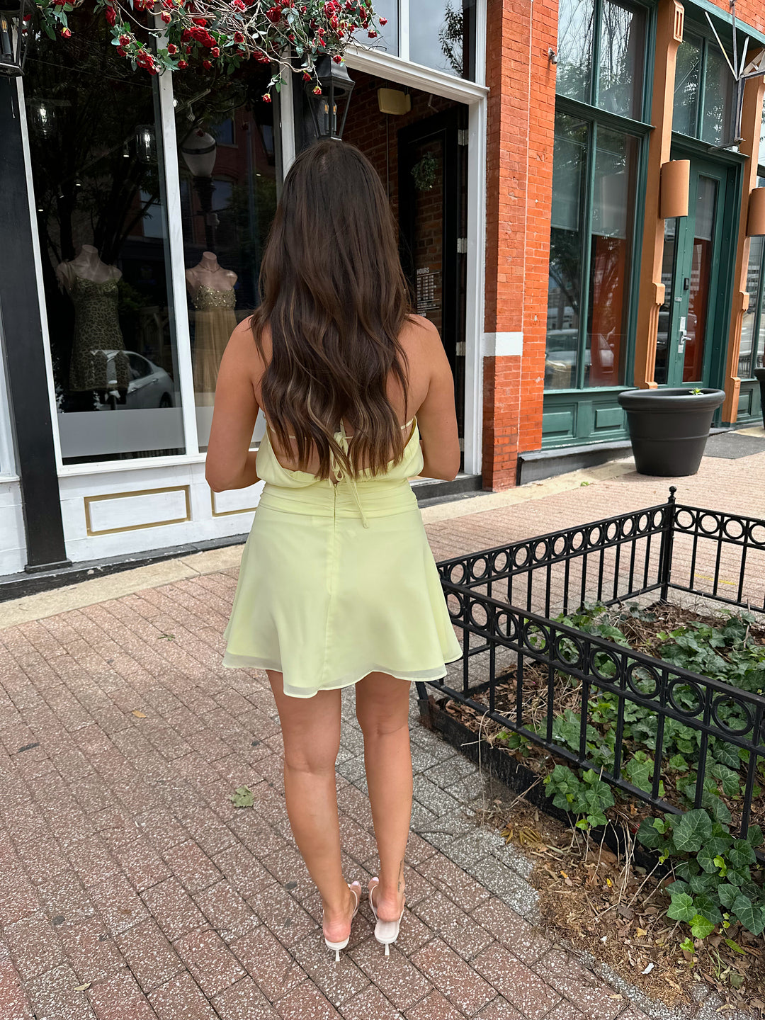 Woman wearing yellow chiffon halter mini dress with beaded detailing, open back with strap detail. 