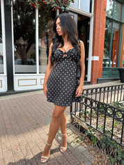 Woman wearing black polka dot mini dress with self tie straps and cutout detail.