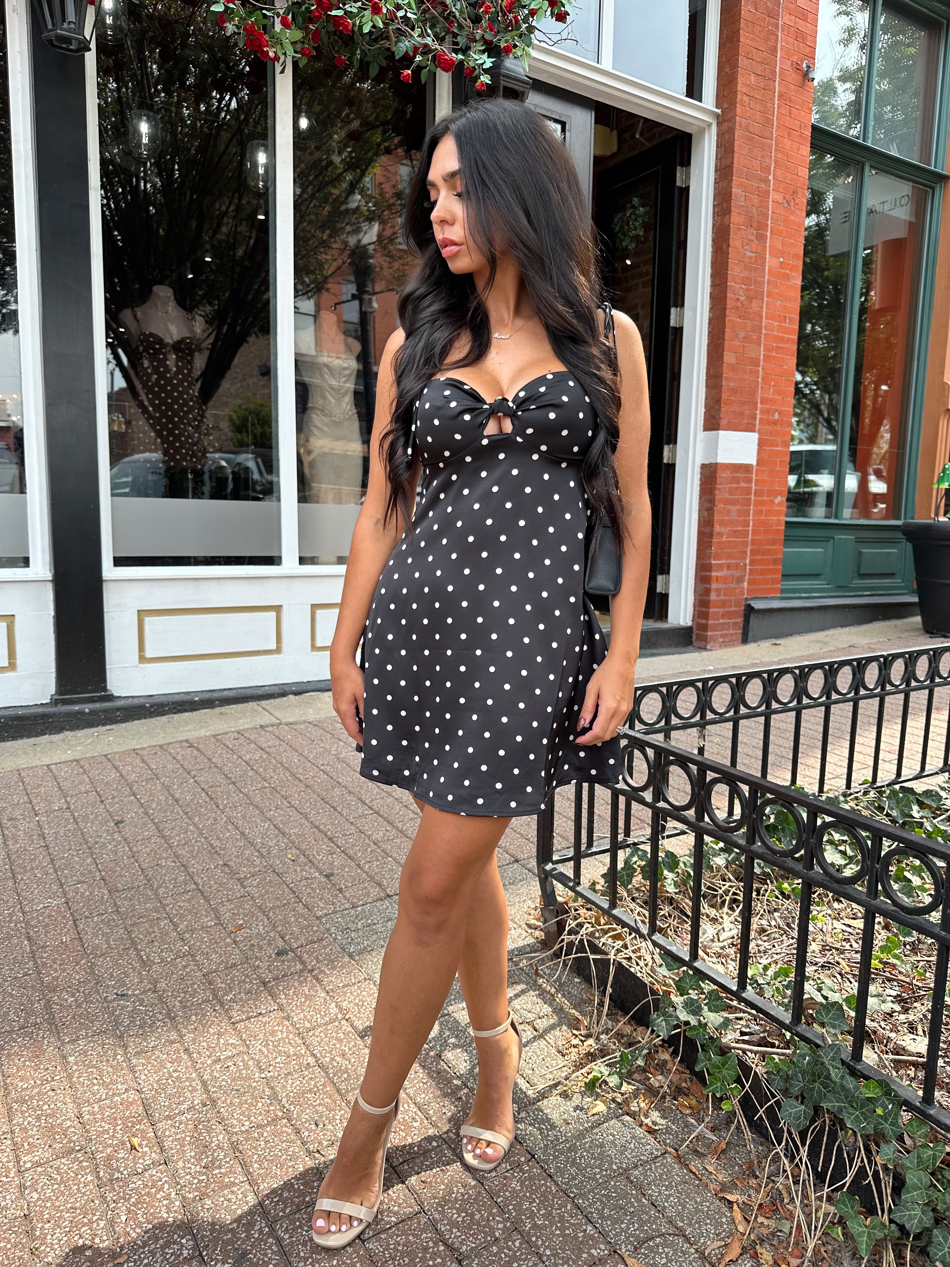 Woman wearing black polka dot mini dress with self tie straps and cutout detail.