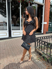 Woman wearing black polka dot mini dress with self tie straps and cutout detail.
