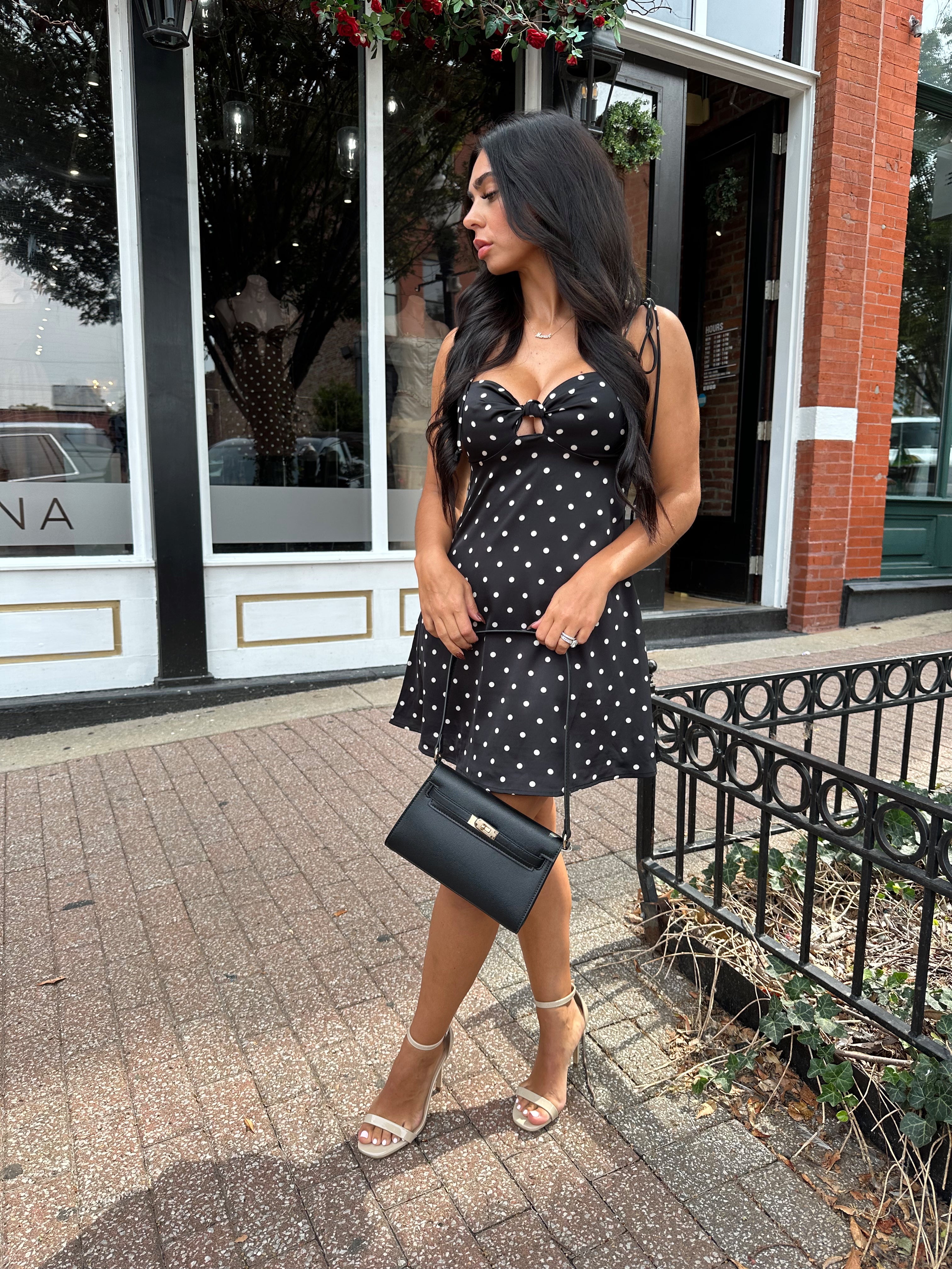 Woman wearing black polka dot mini dress with self tie straps and cutout detail.