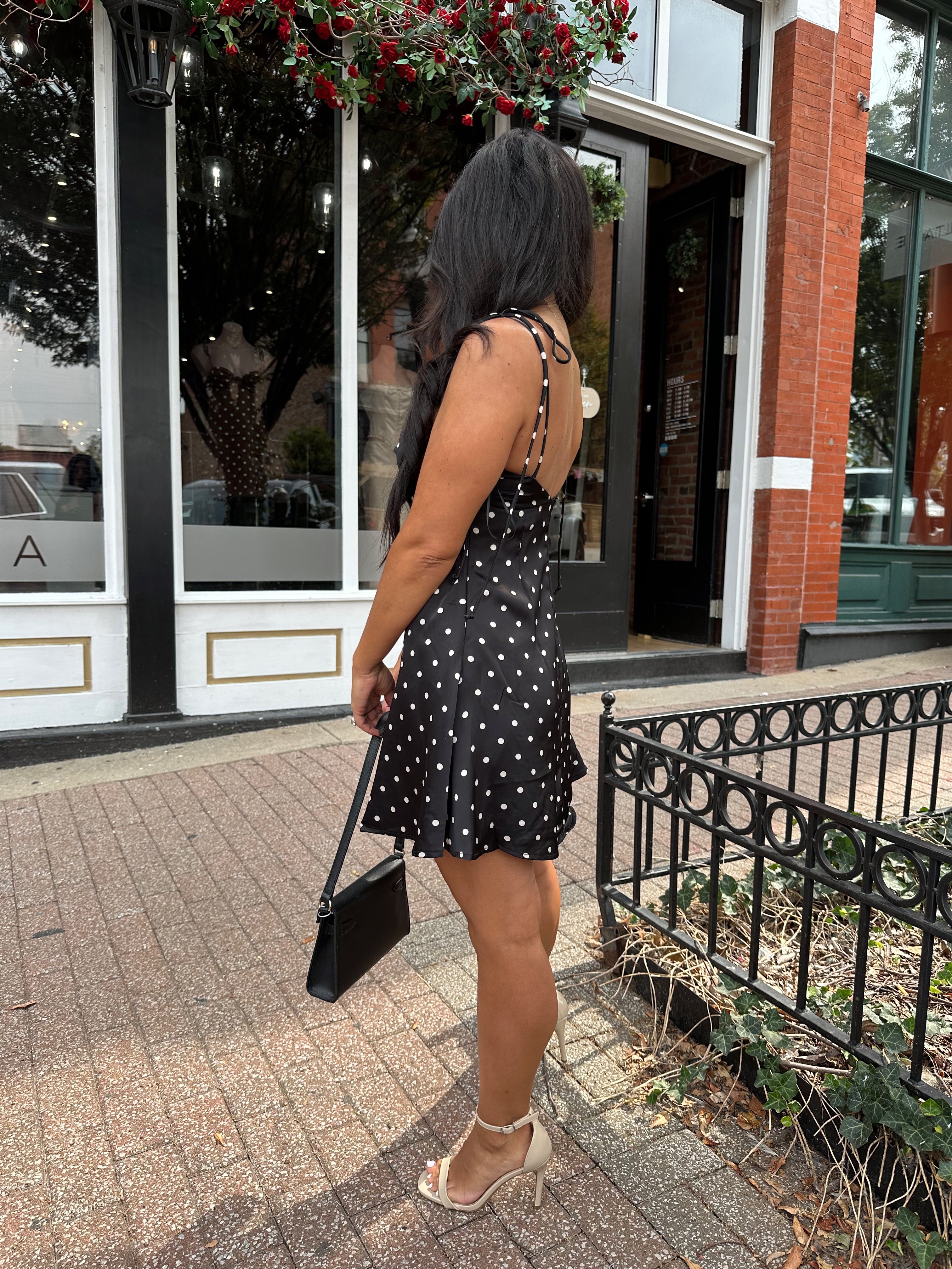 Woman wearing black polka dot mini dress with self tie straps and cutout detail.